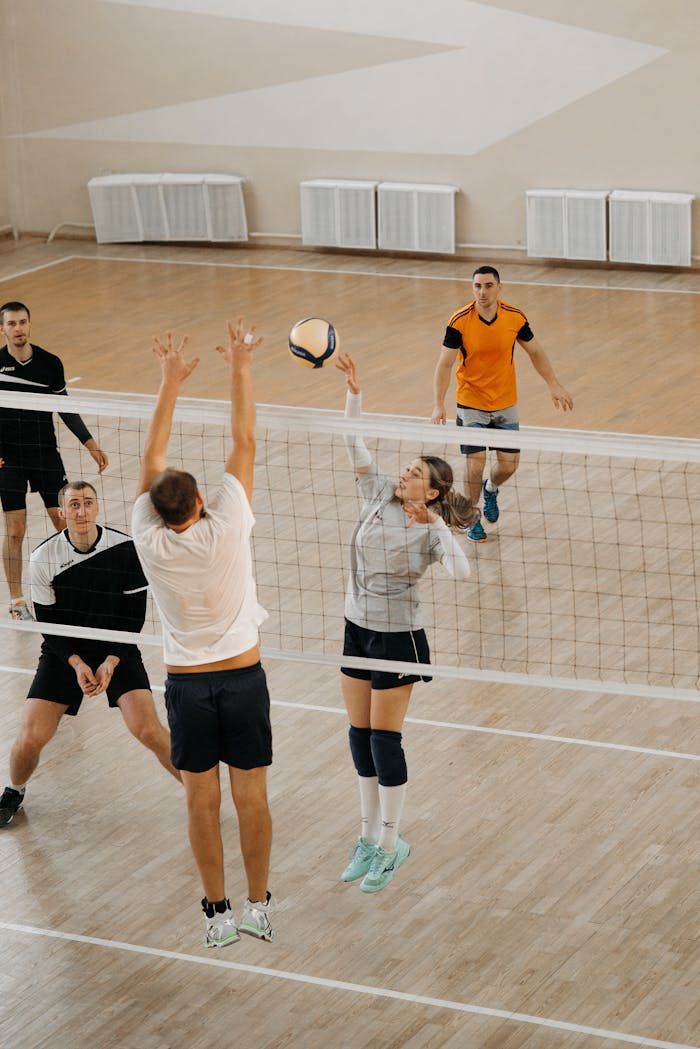 Men and women athletes competing fiercely in an indoor volleyball match with dynamic action on the court.